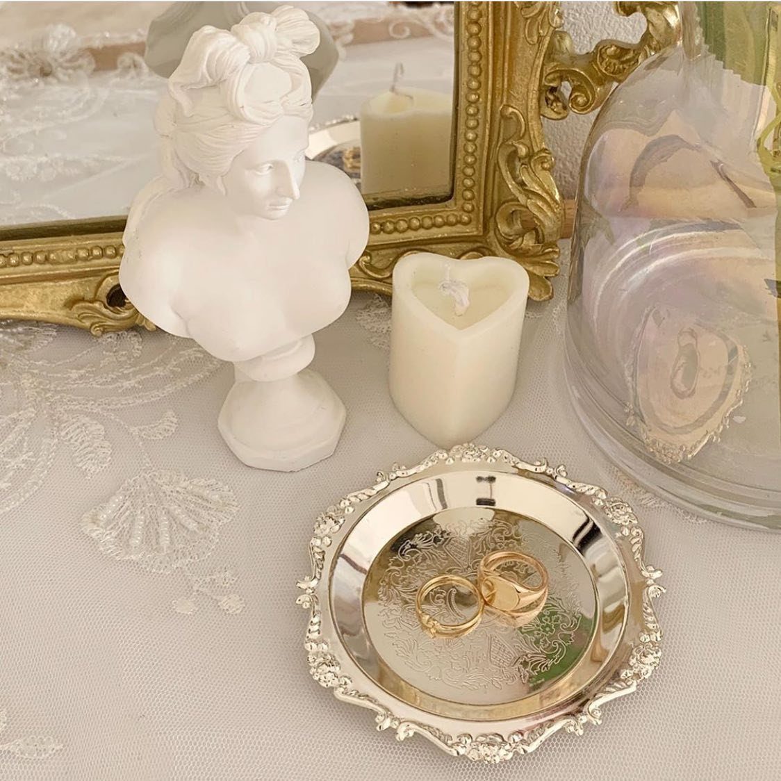 Small silver tray with gold rings on a white lace tablecloth near a white bust.