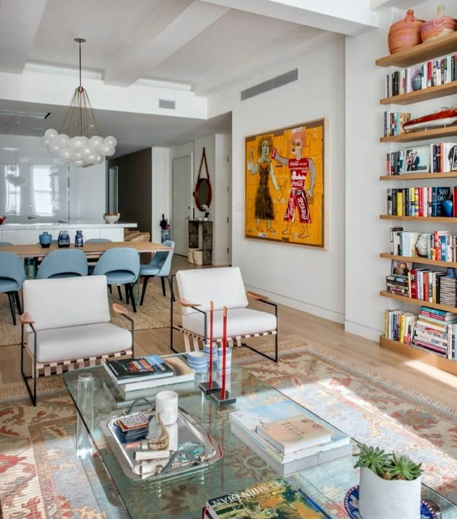 Glass coffee table with stacked books and small plants in a bright, modern living room.