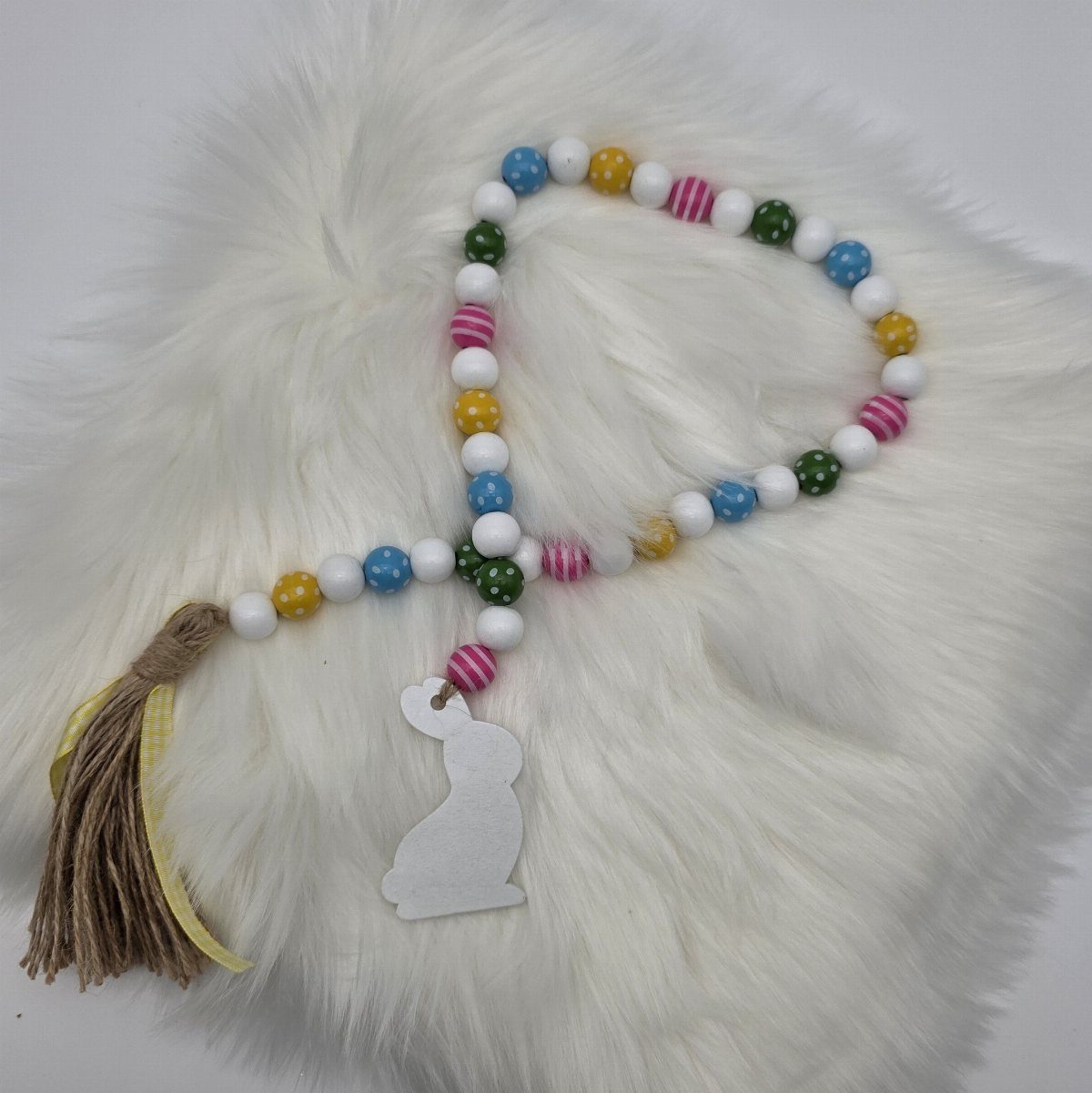 Colorful wooden beads with a tassel and rabbit cutout on white faux fur.