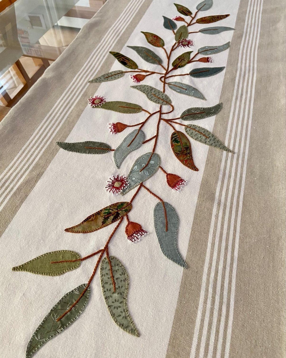 Embroidered botanical fabric runner with green leaves laid on a neutral surface.