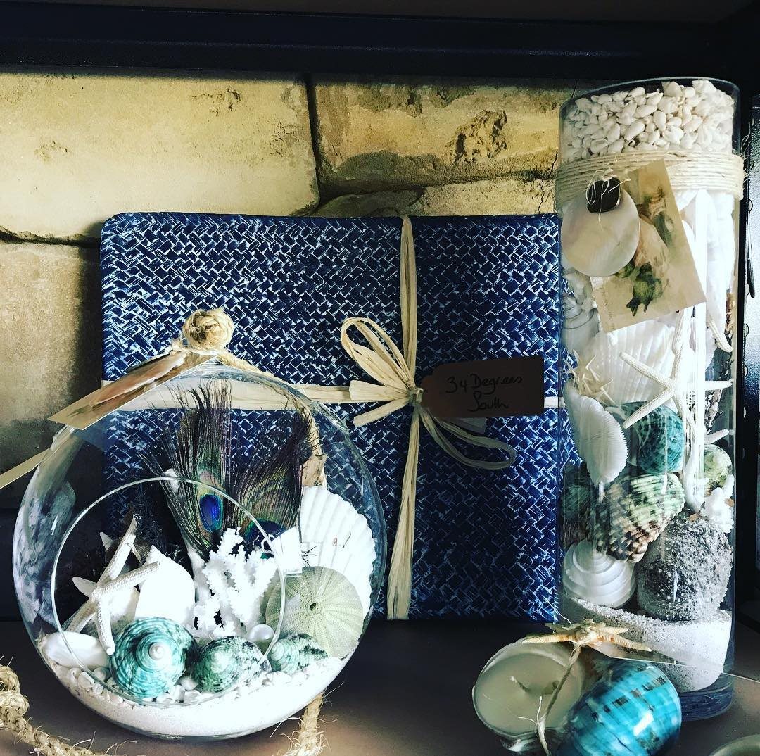 Glass spheres and cylinders filled with seashells, starfish, and pebbles on a stone surface.