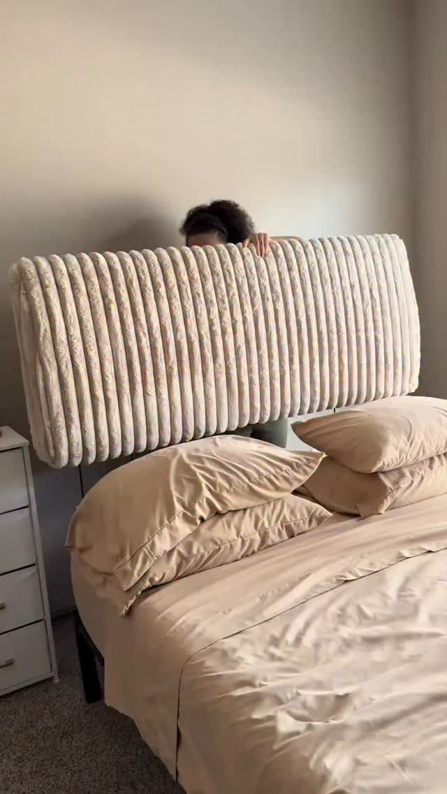A beige ribbed fabric headboard on a bed with tan linens and pillows.