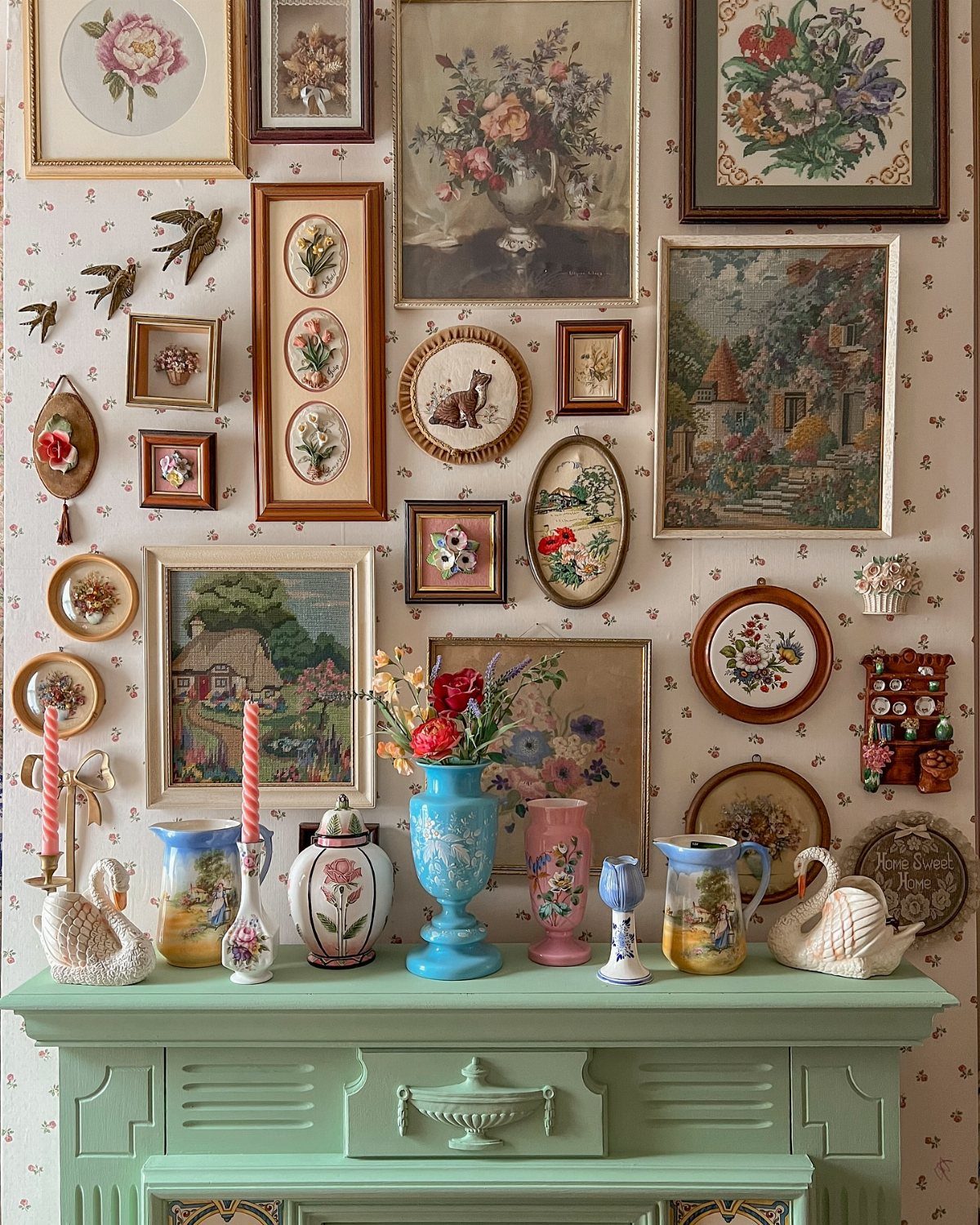 Vintage framed botanical art and floral plates displayed on a patterned wall above a mint green sideboard.