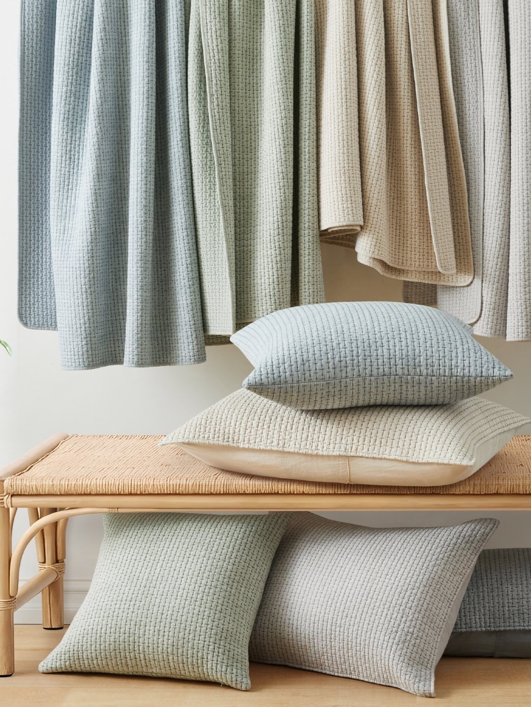Textured fabric swatches and matching pillows arranged on and around a rattan bench.