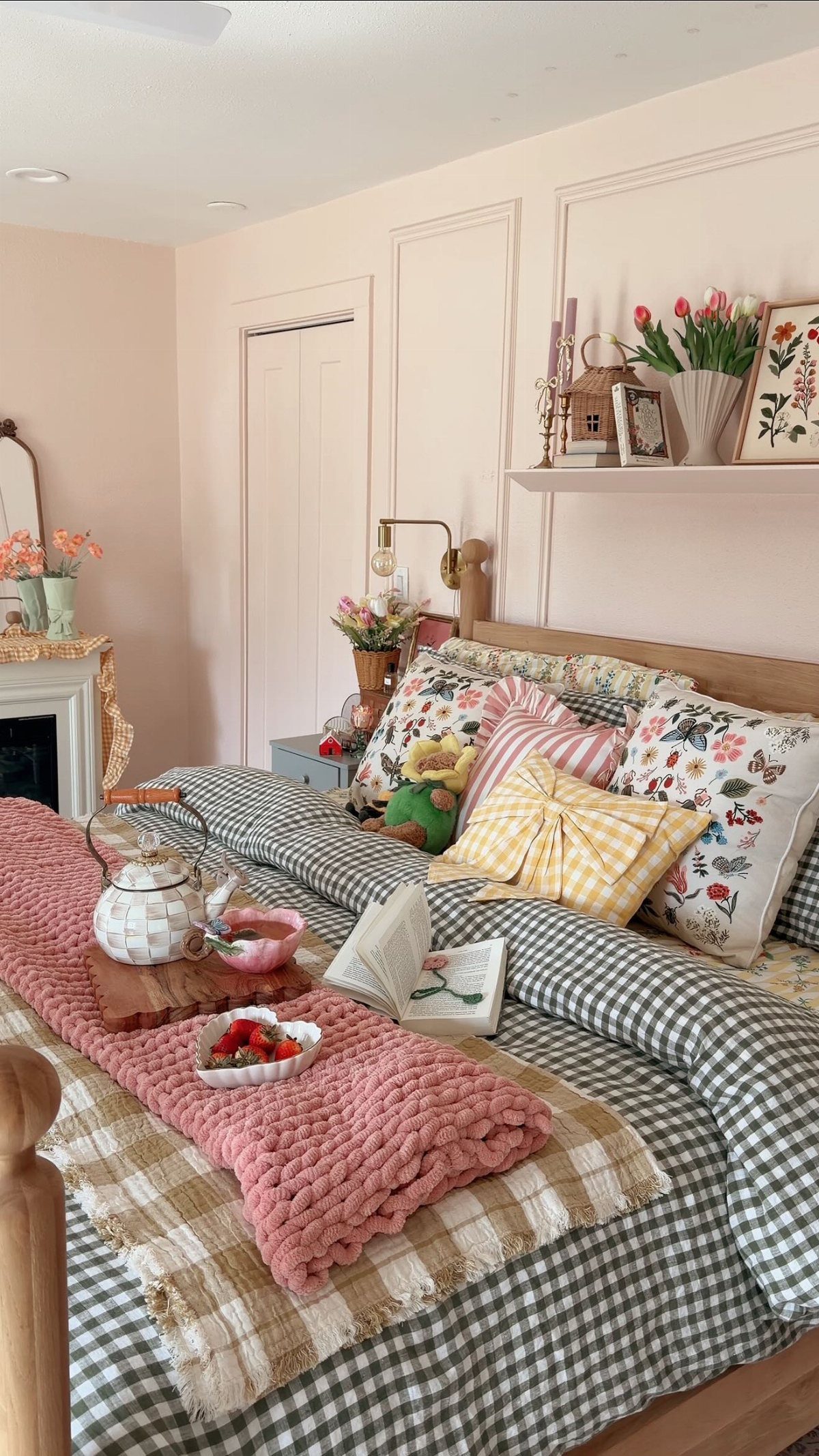 A cozy bed with gingham bedding, floral pillows, and a pink knit throw blanket.