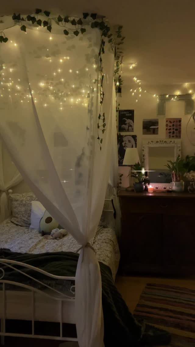 White canopy bed with sheer fabric, ivy vines, and twinkling fairy lights in a cozy bedroom.