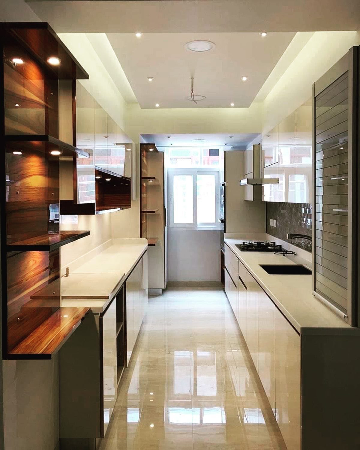 A narrow galley kitchen featuring white cabinetry and dark wood open shelving with warm lighting.