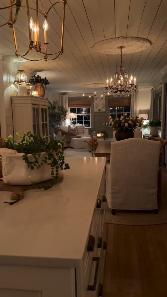 Warmly lit kitchen and living space with chandeliers, white cabinetry, and cozy neutral furniture.