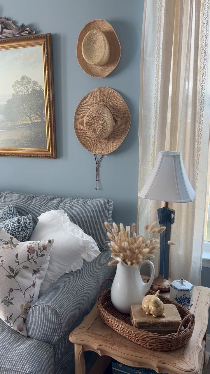 Blue sofa with decorative pillows next to a wooden side table with a lamp and dried flowers.