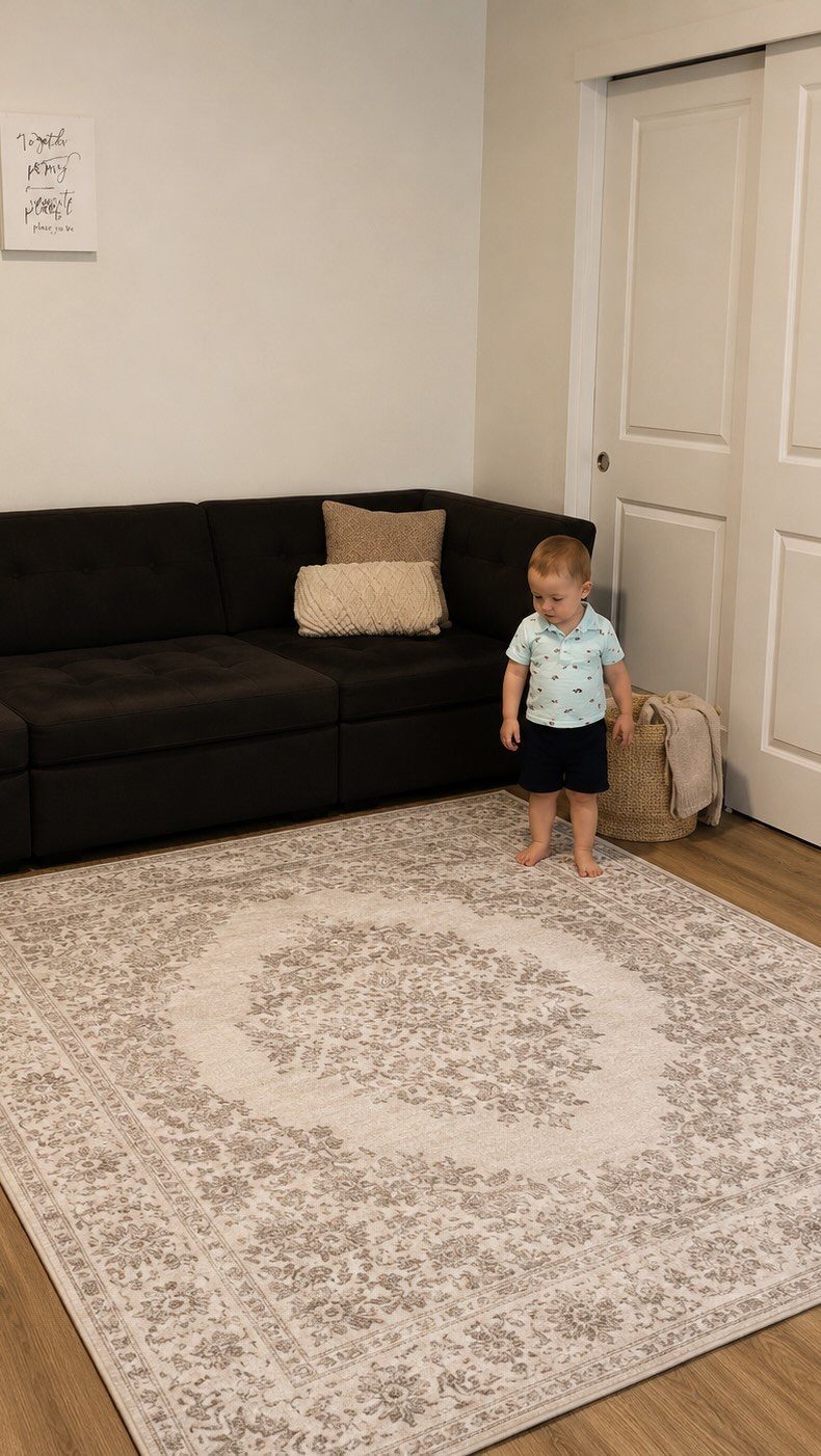A patterned beige area rug on a wooden floor in front of a black sofa.