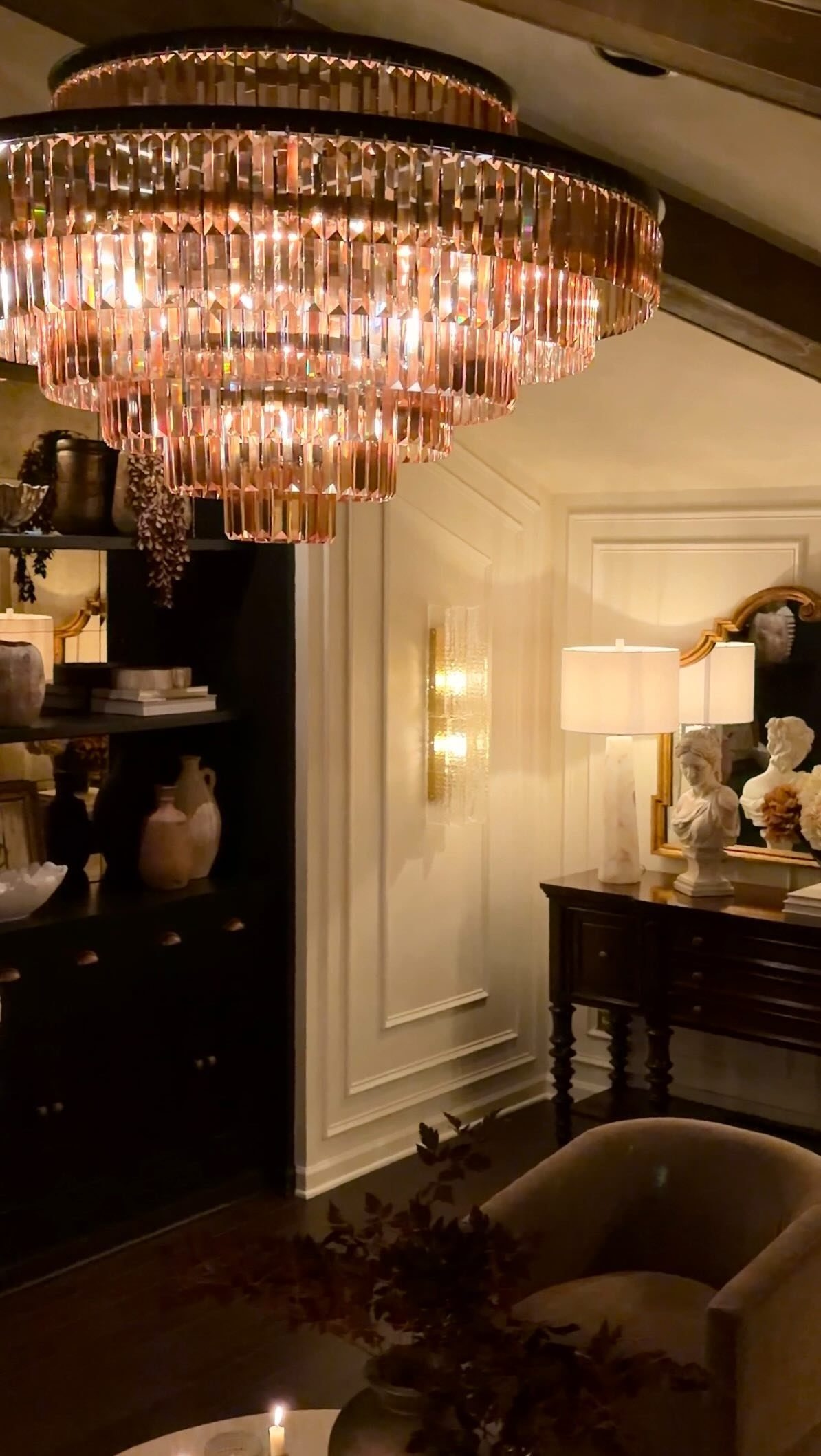 A glowing amber crystal chandelier hangs above a dark wooden sideboard and white paneled walls.