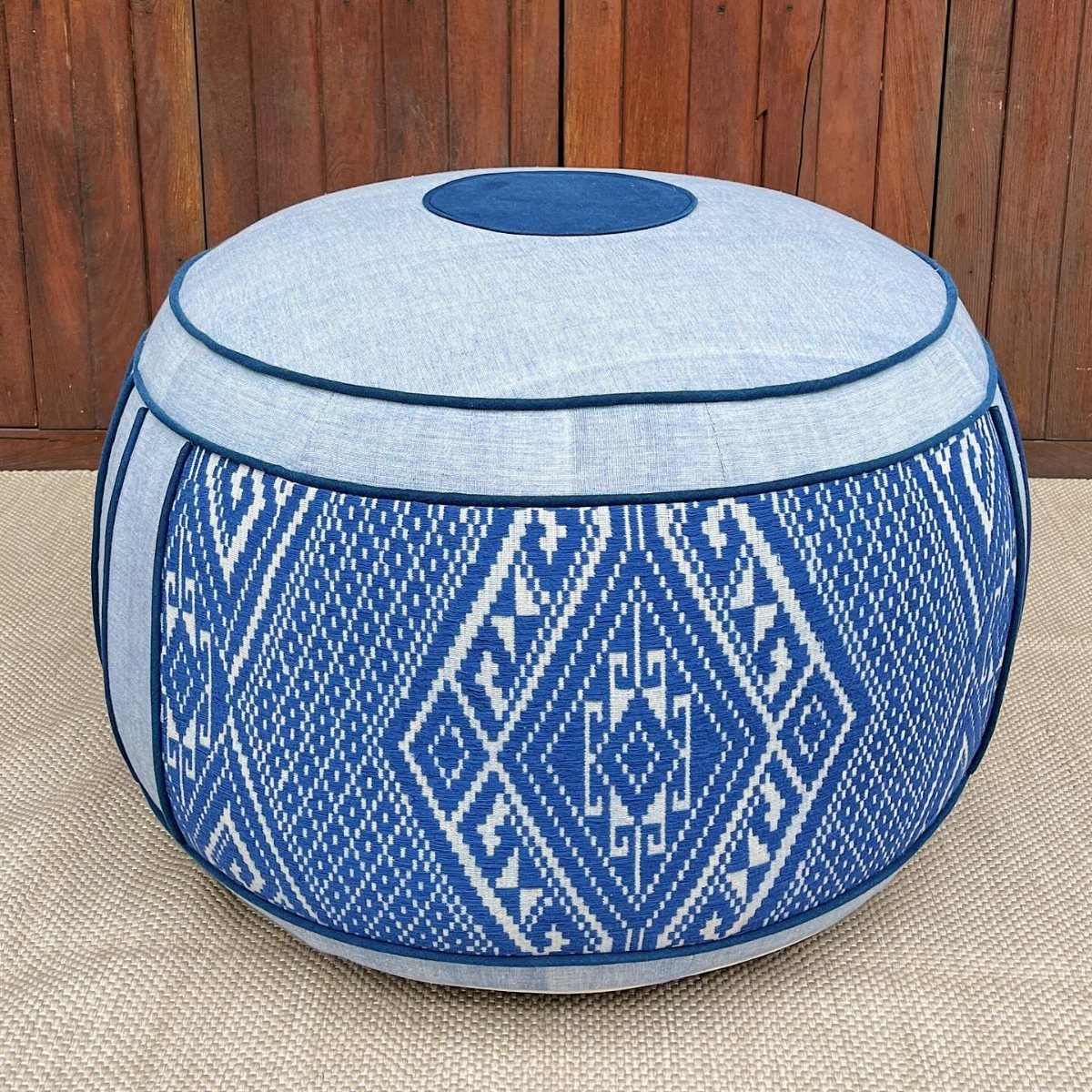 A round blue and white patterned pouf resting on a beige textured surface.