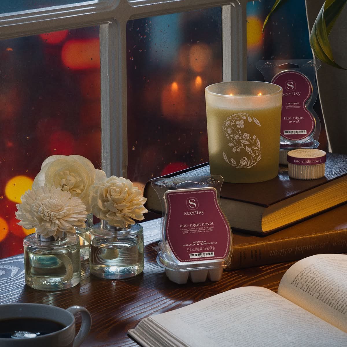 A lit scented candle on a book next to an open book and white flowers.