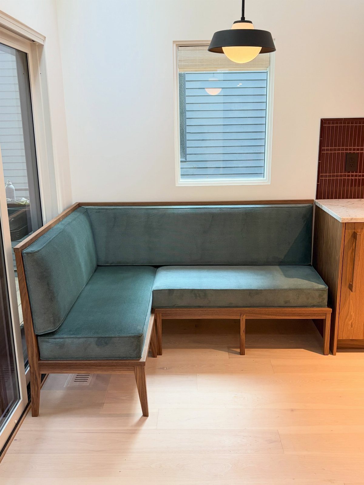 A teal velvet L-shaped banquette with a wooden frame on light wood floors.
