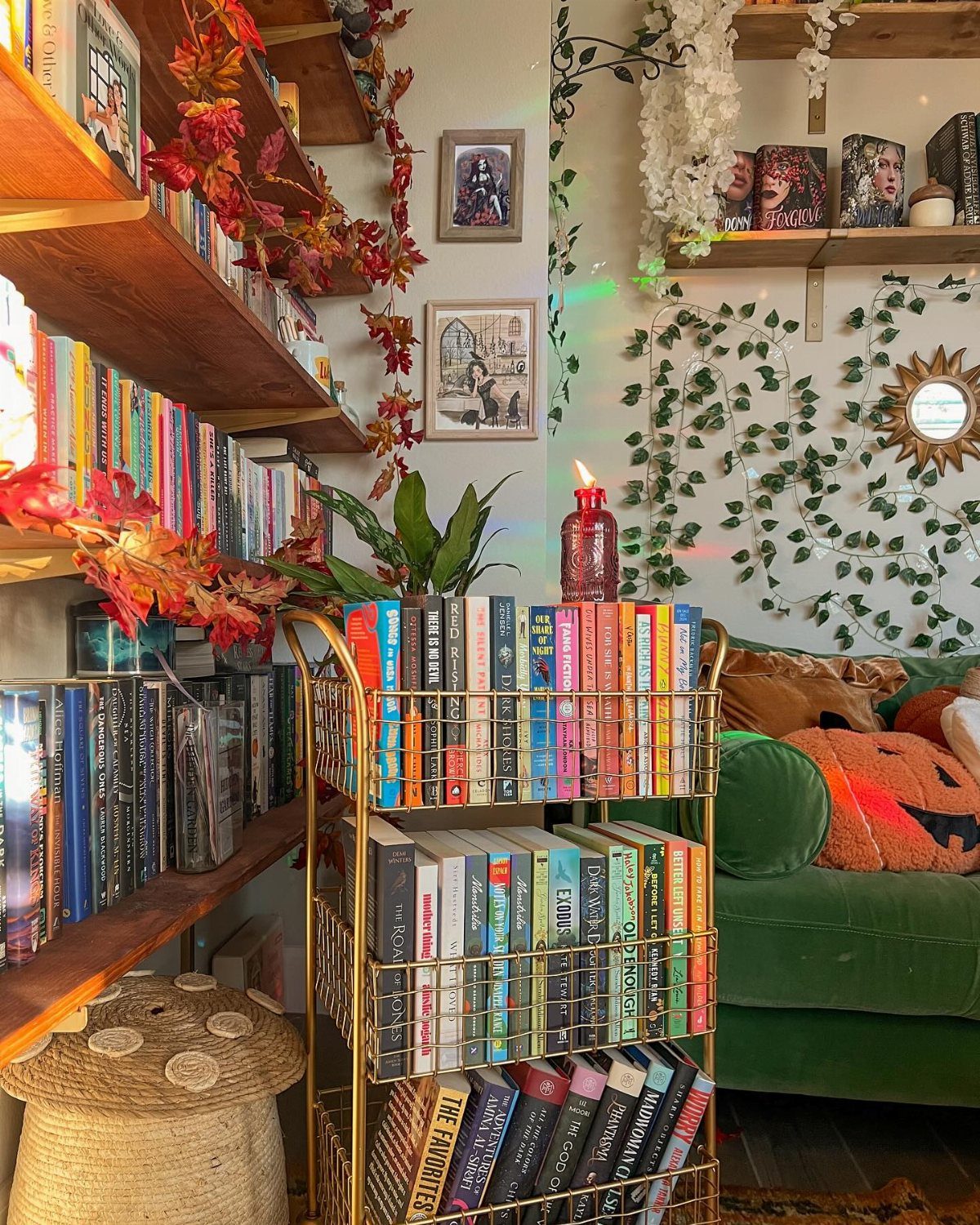 A cozy reading nook with a green sofa, gold book cart, and autumn leaf decorations.