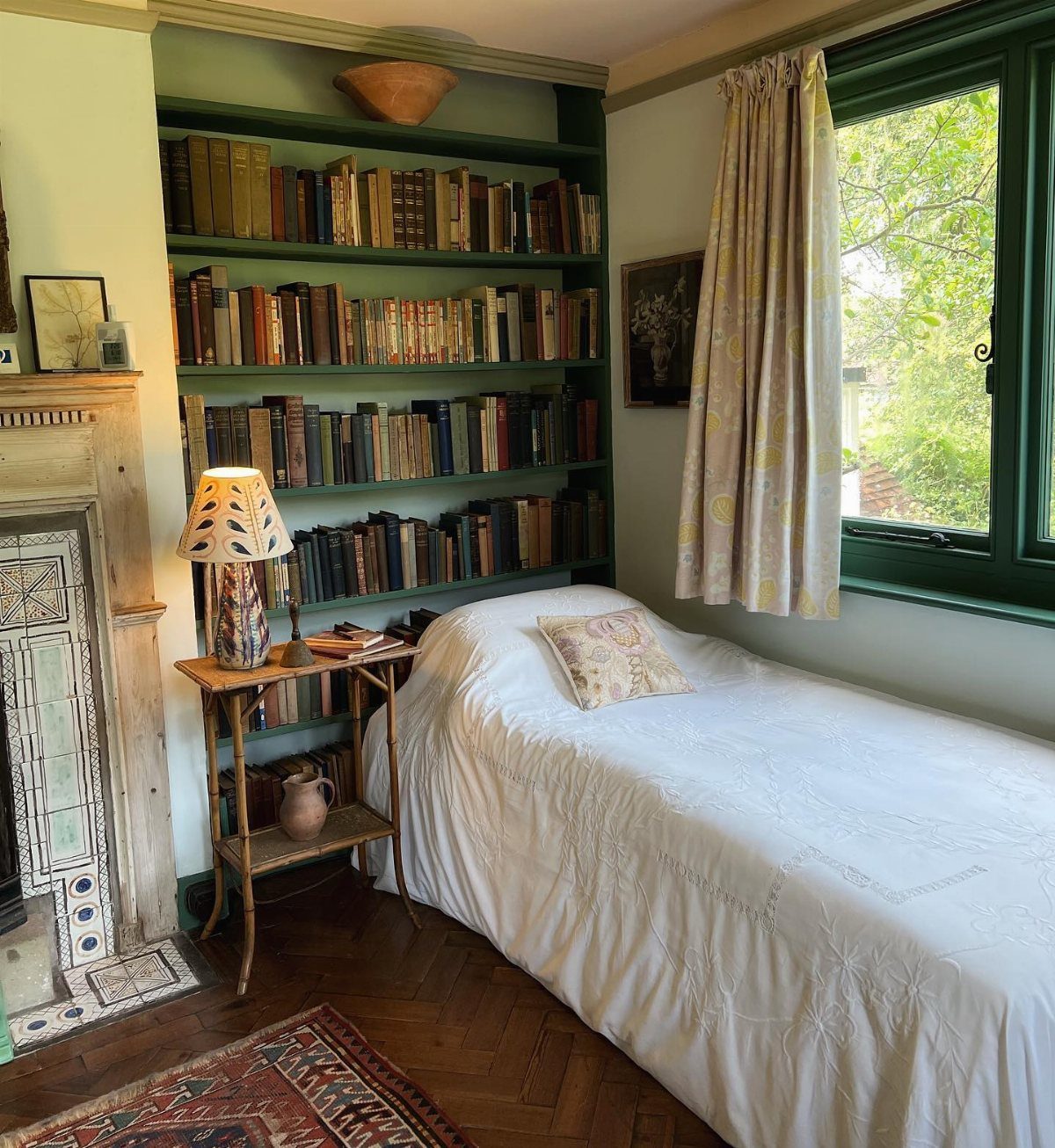 A white bed positioned against a large teal built-in bookcase filled with many books.