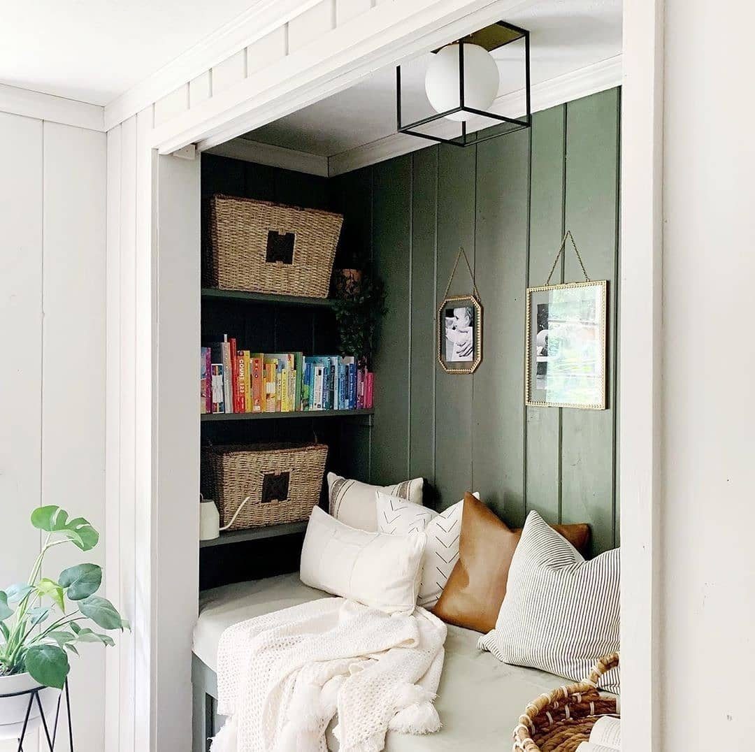A cozy reading nook built into a closet with green walls, cushions, and bookshelves.