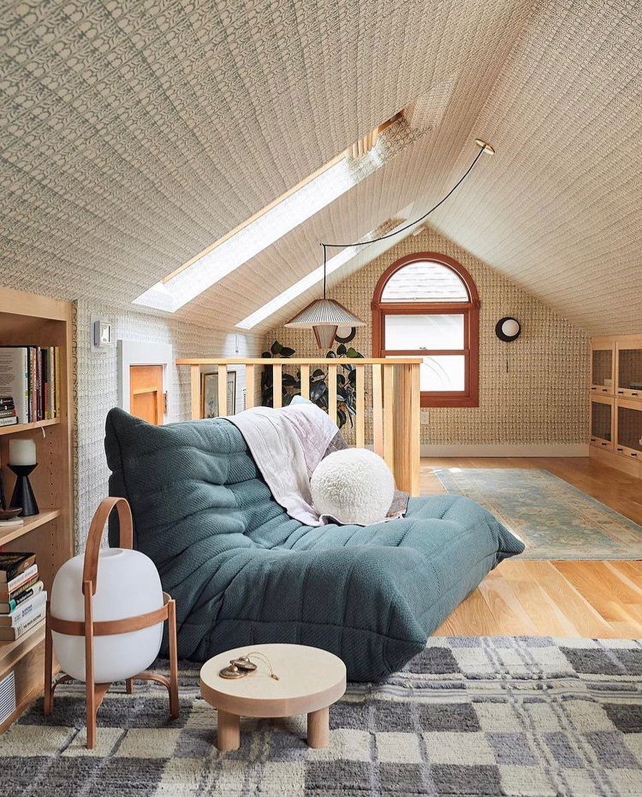 A teal tufted floor sofa sits on a wooden floor with a plaid rug and small side table.