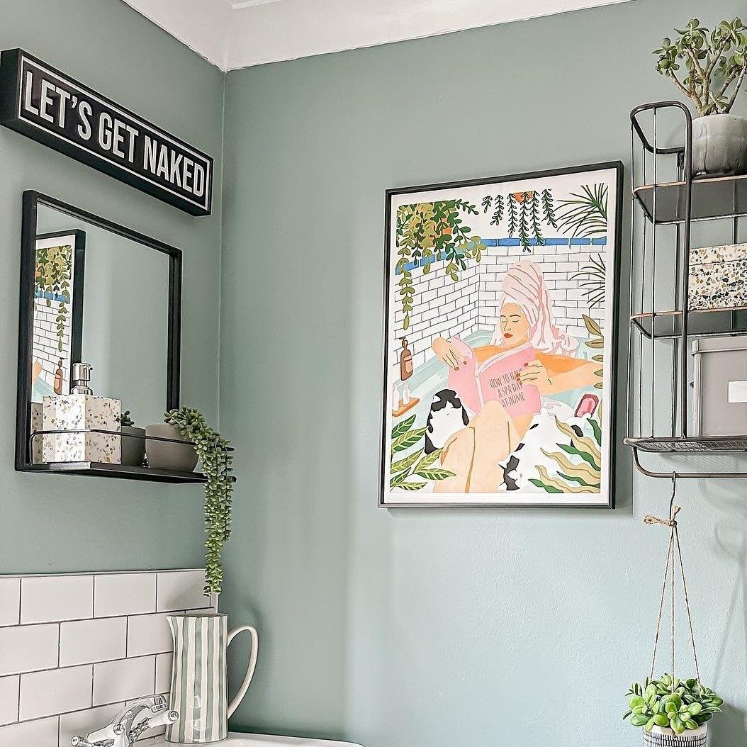 Framed colorful illustration of a woman reading on a light green bathroom wall.