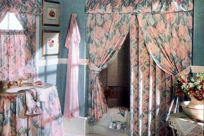 Floral pink and green curtains hanging over a window and a doorway in a blue bathroom.