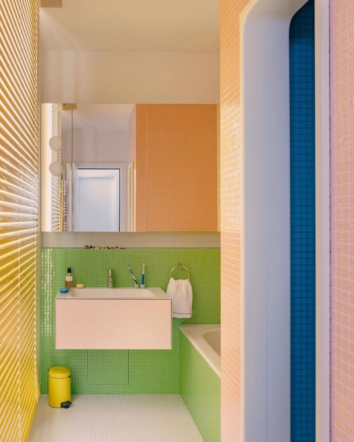 Green mosaic tiles covering bathroom walls next to a white sink and bathtub.
