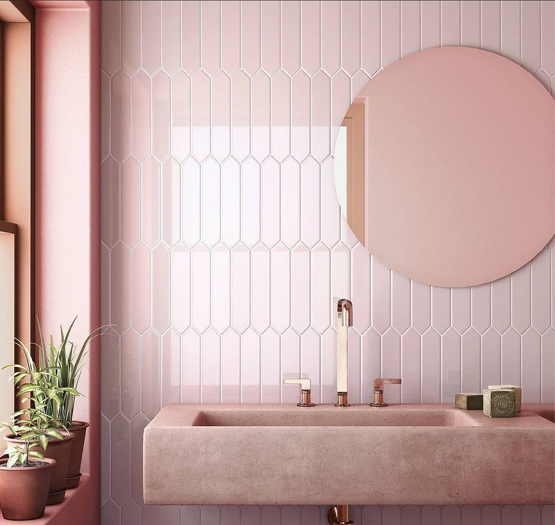 Pink elongated tiles on a bathroom wall with a stone sink and round mirror.