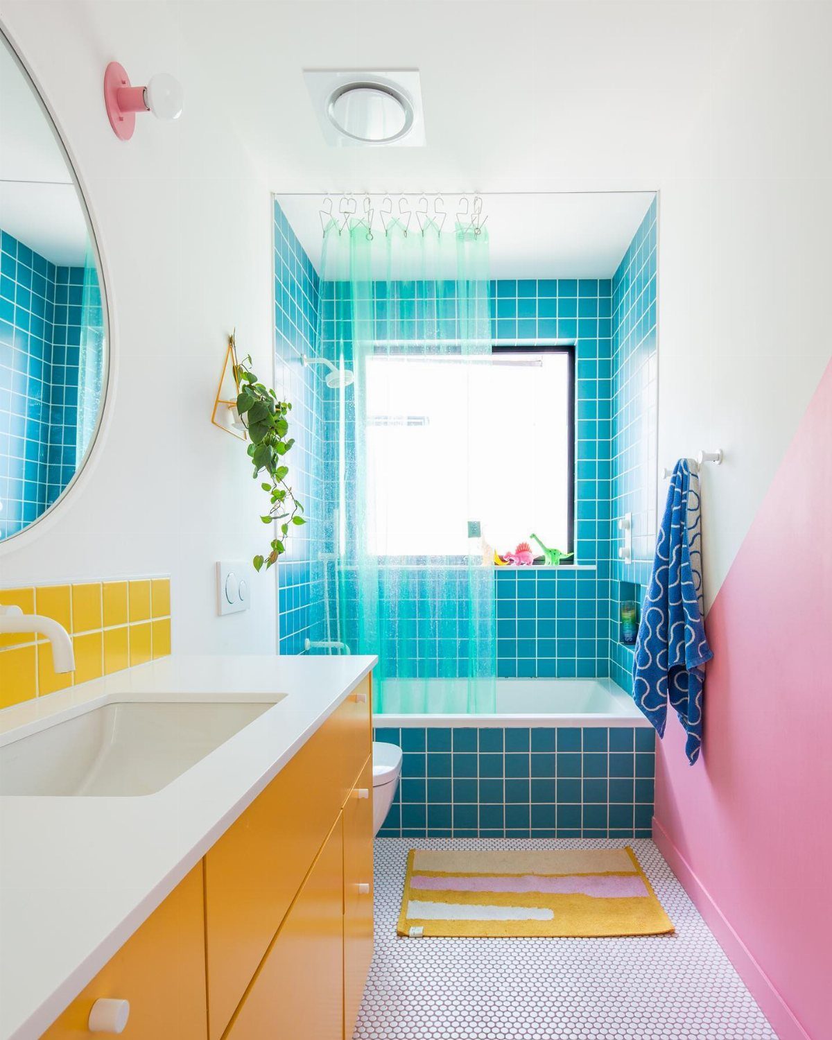 A colorful bathroom with teal tiles, pink walls, and bright yellow vanity cabinets.
