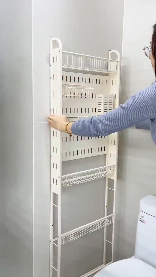 A person installing a tall white wire storage rack against a grey bathroom wall.
