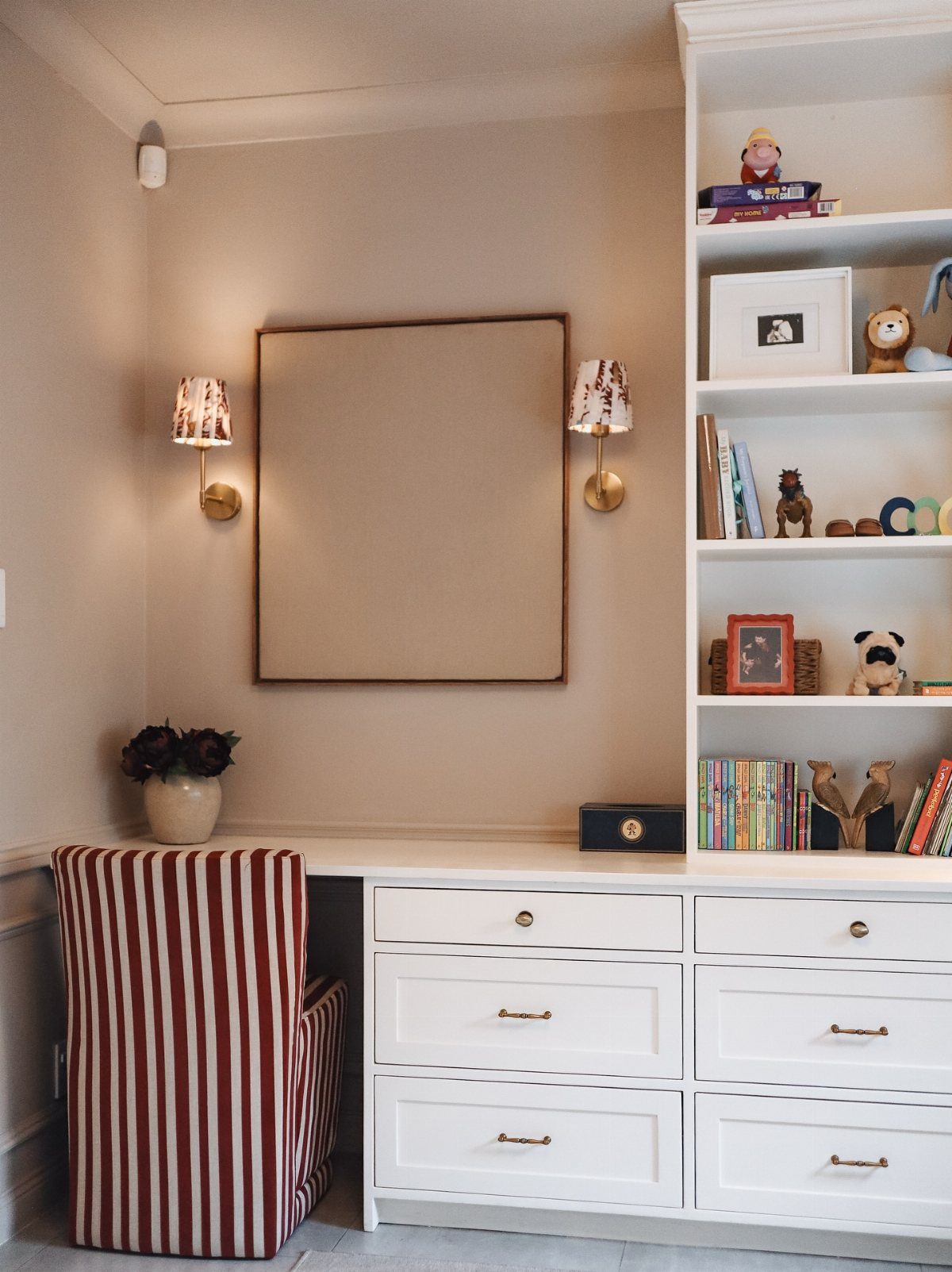 A white desk with a striped chair, a bookshelf, and a large mirror on the wall.
