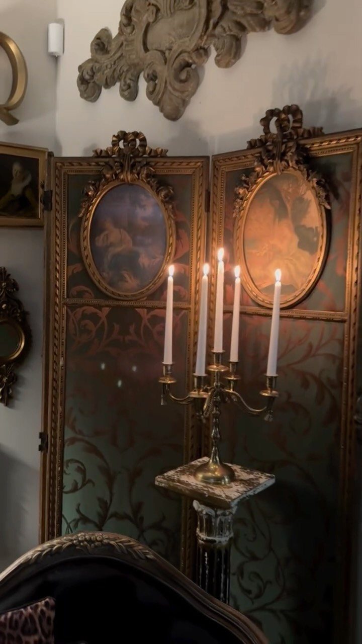 A lit gold candelabra stands before an ornate dark folding screen with classical paintings.