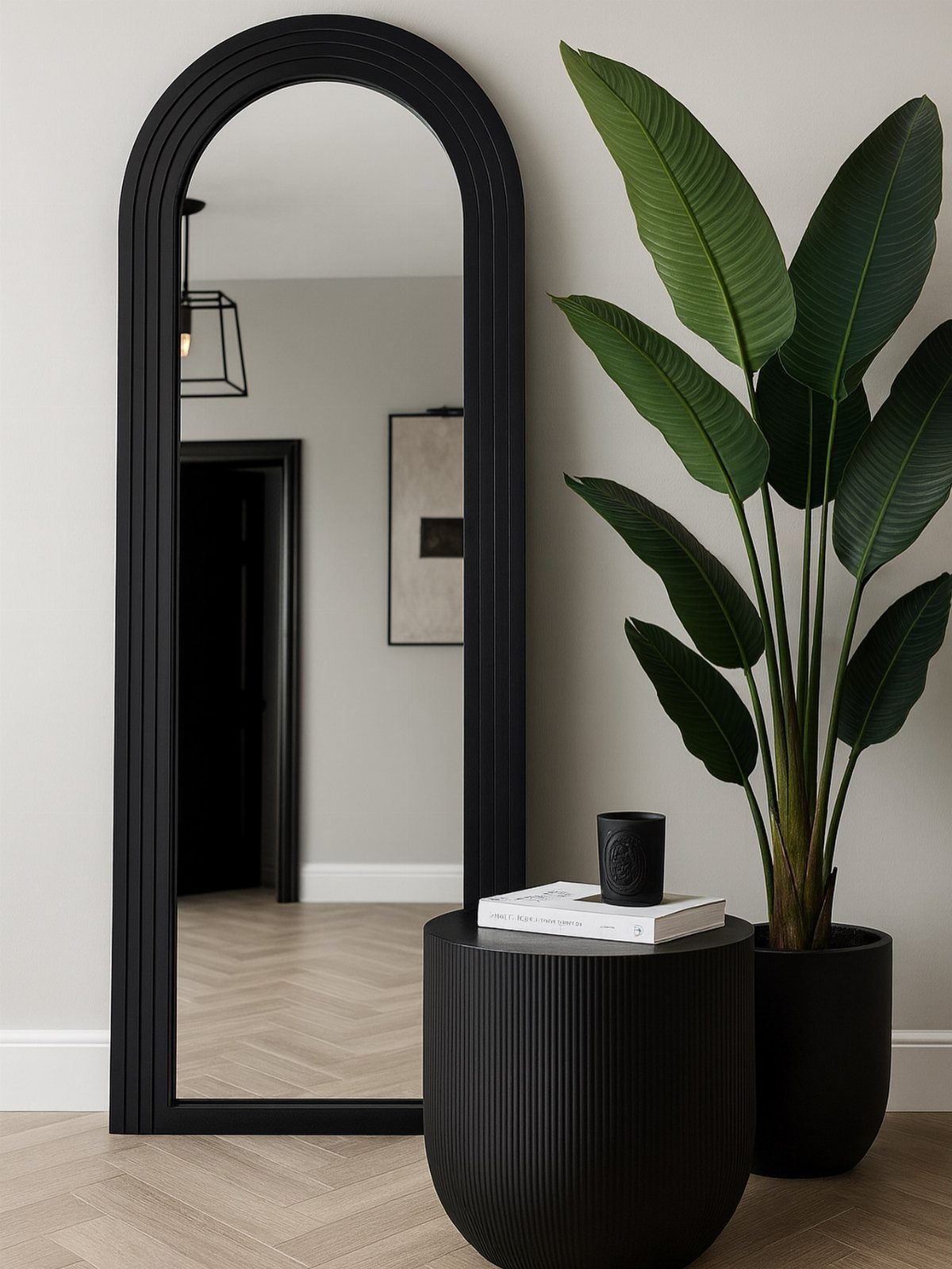 Large black arched floor mirror standing next to a potted plant and a black side table.