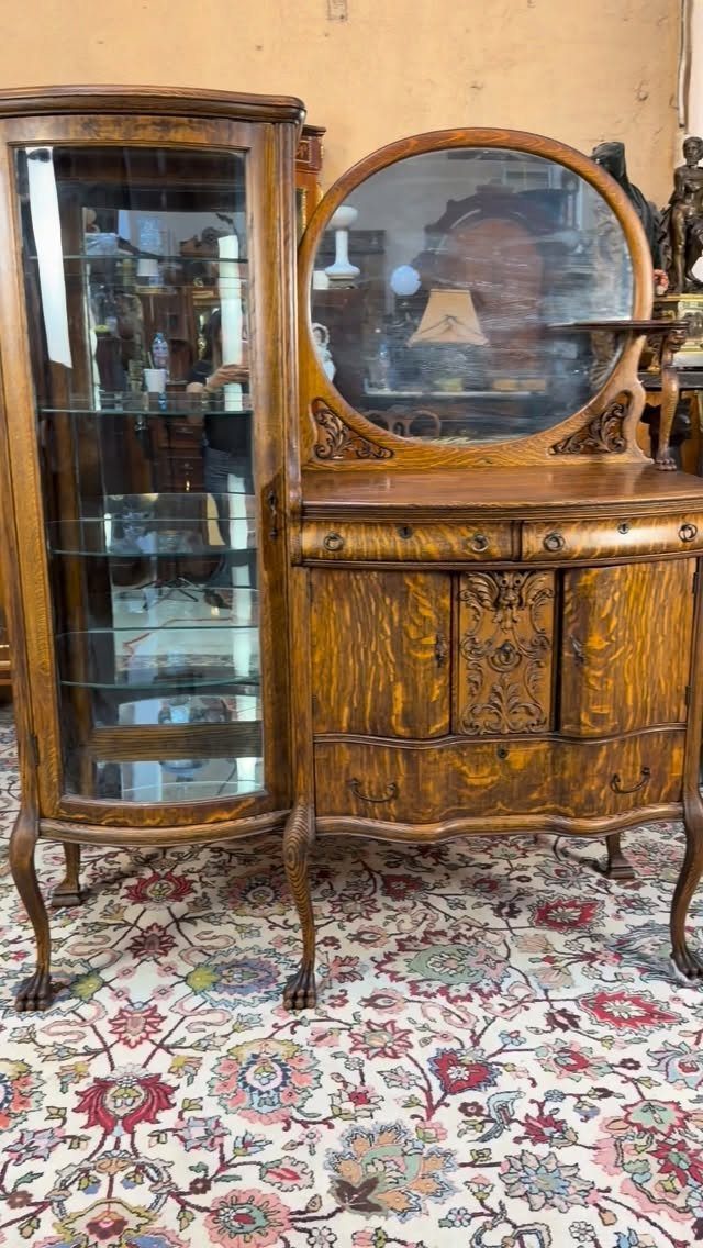 Ornate dark wood vintage sideboard with a glass display cabinet and an oval mirror.