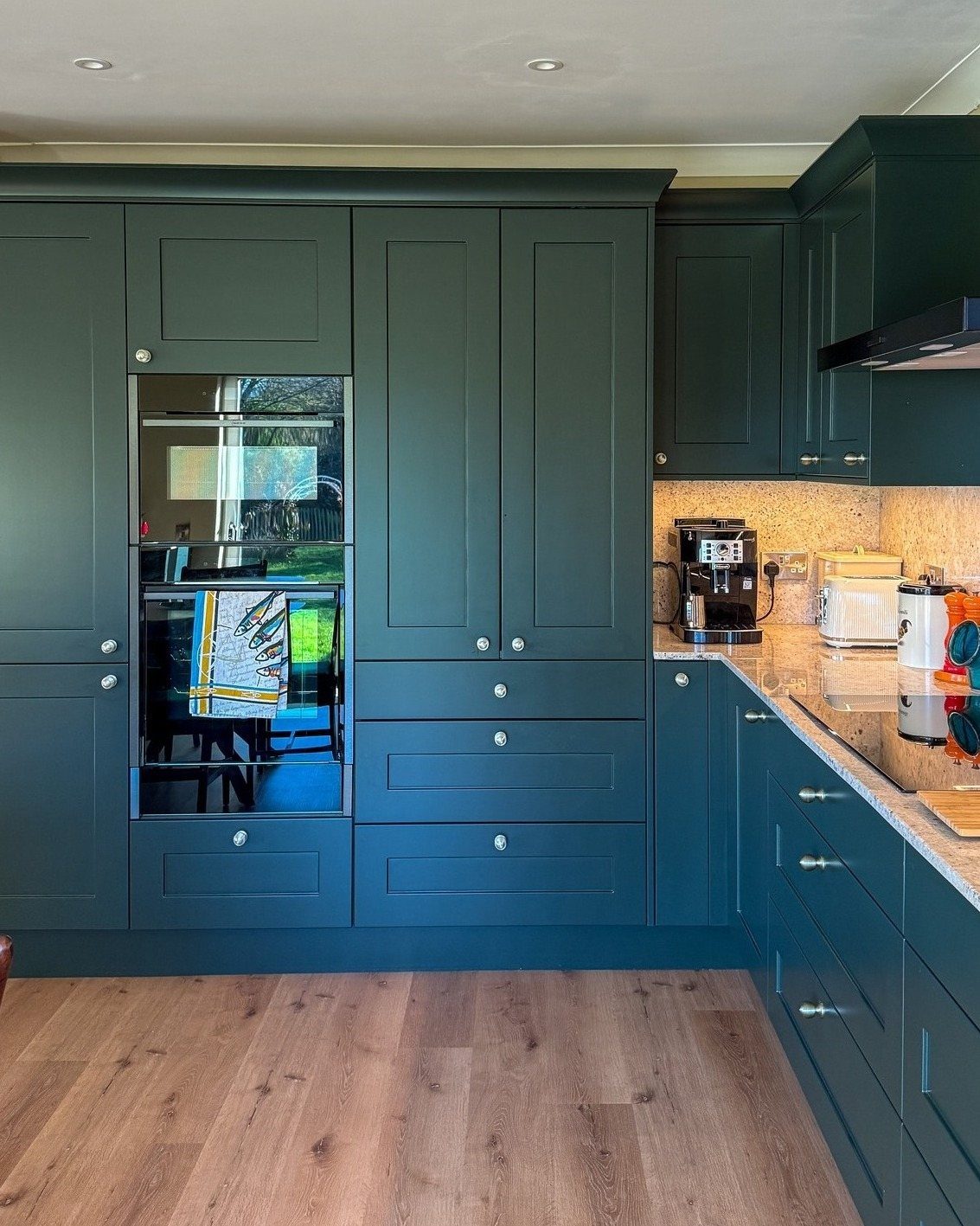 Dark green kitchen cabinets with pale quartz worktops and a built-in oven.