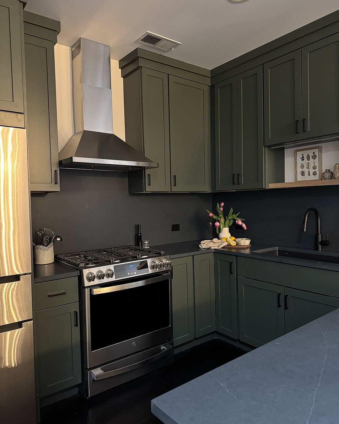 Charcoal green kitchen cabinets with stainless steel appliances and dark countertops in a modern setting.