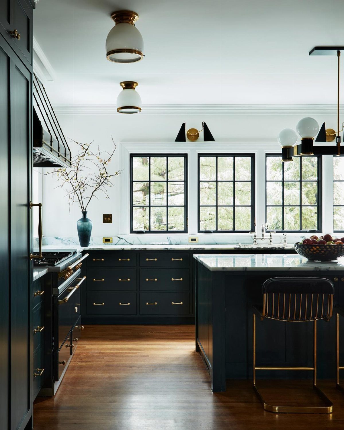 Dark green kitchen cabinets with white marble countertops and gold hardware in a bright room.