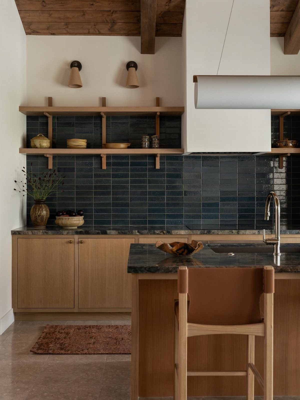 Kitchen with light wood cabinetry, dark teal tile backsplash, and stone countertops.