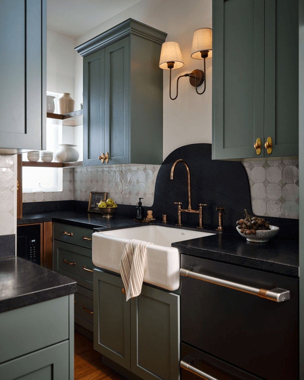 Dark green shaker cabinets with black countertops and a white farmhouse sink in a kitchen.