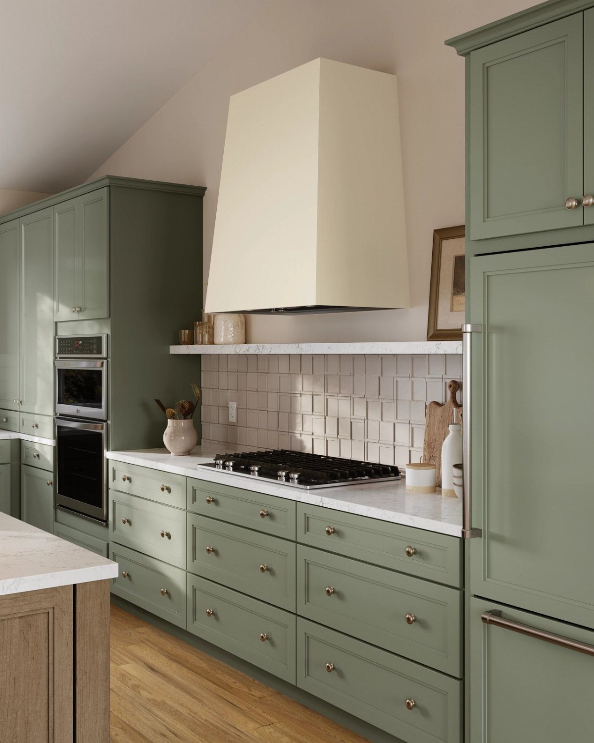 Muted moss green kitchen cabinets with white marble countertops and a cream range hood.