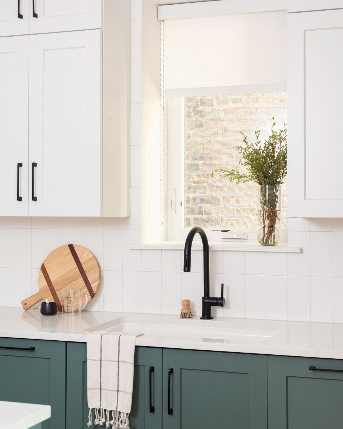 Dark green lower kitchen cabinets paired with white upper cabinets and a white tiled backsplash.