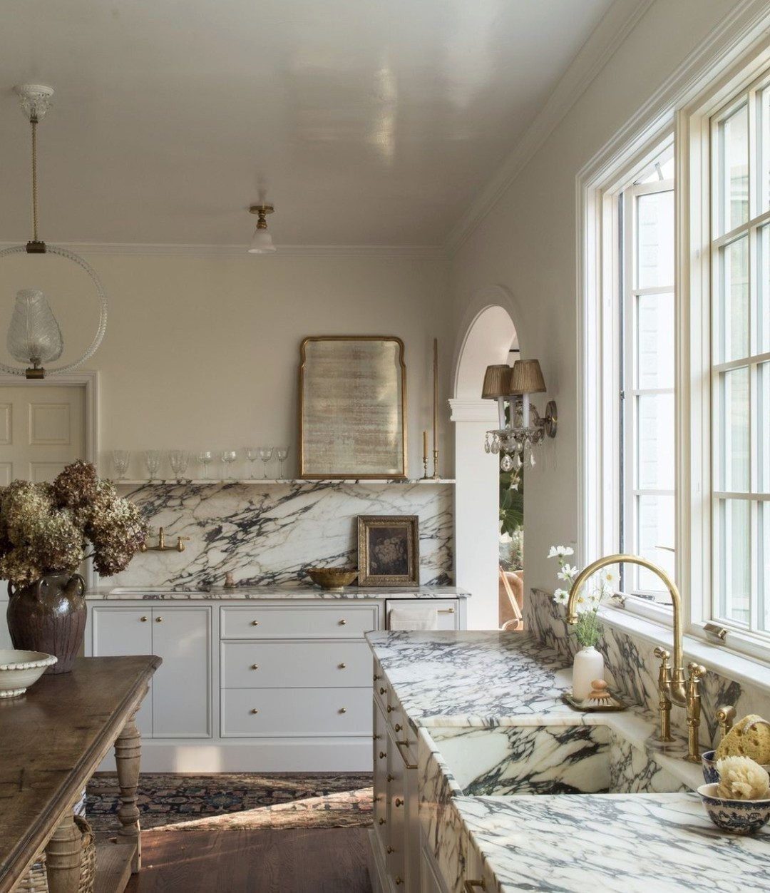 Marble countertops and backsplash in a bright kitchen with white cabinets and wooden furniture.