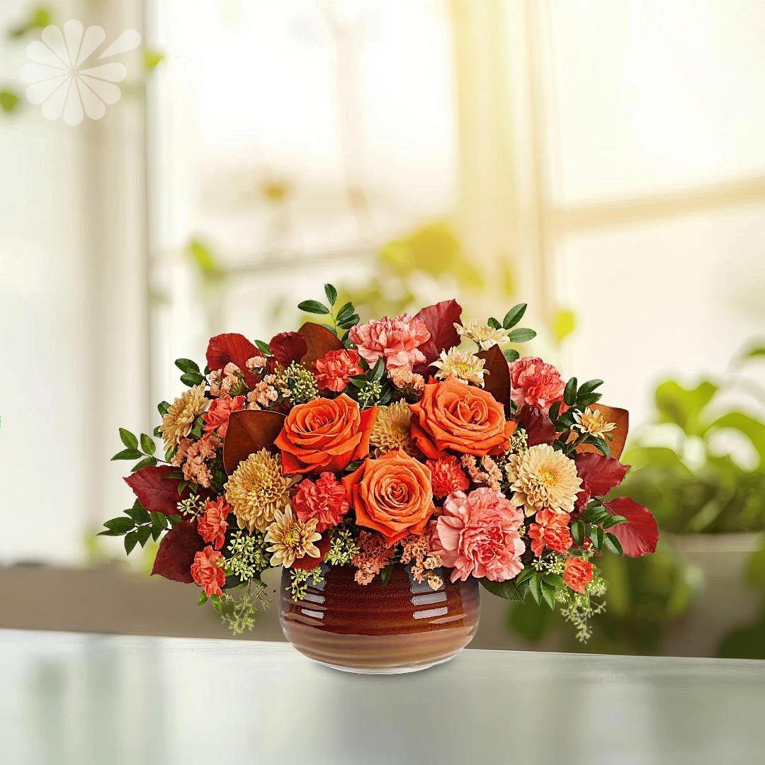 Orange roses and pink carnations arranged in a round ceramic vase on a table.
