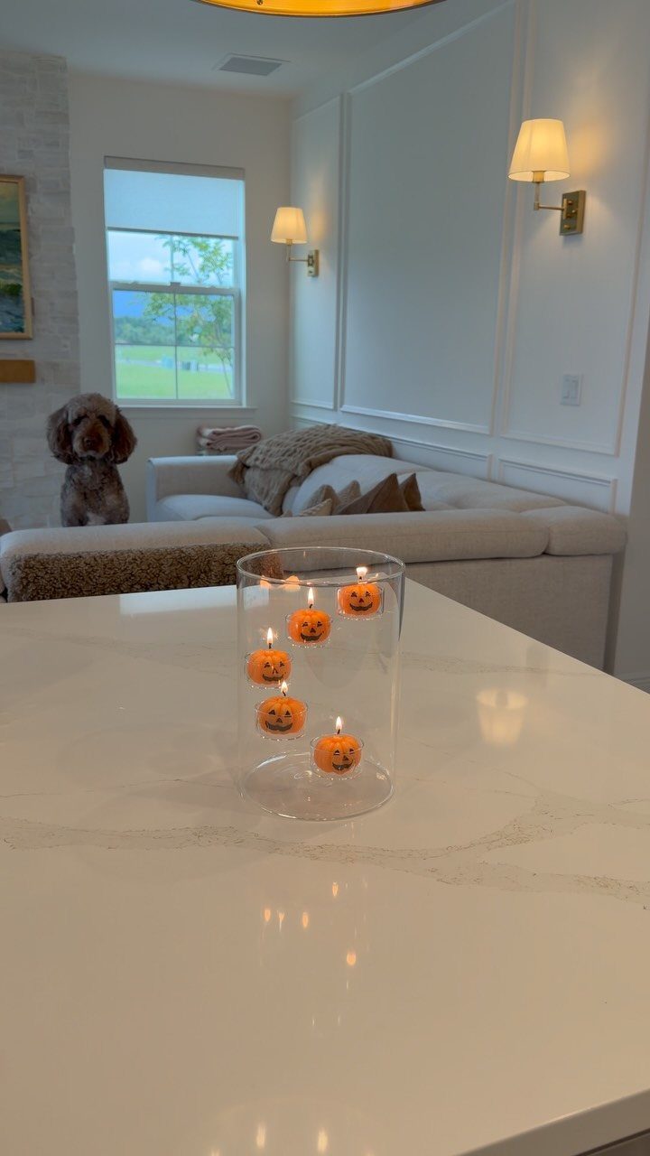 Floating pumpkin candles in a clear glass vase on a white marble countertop.