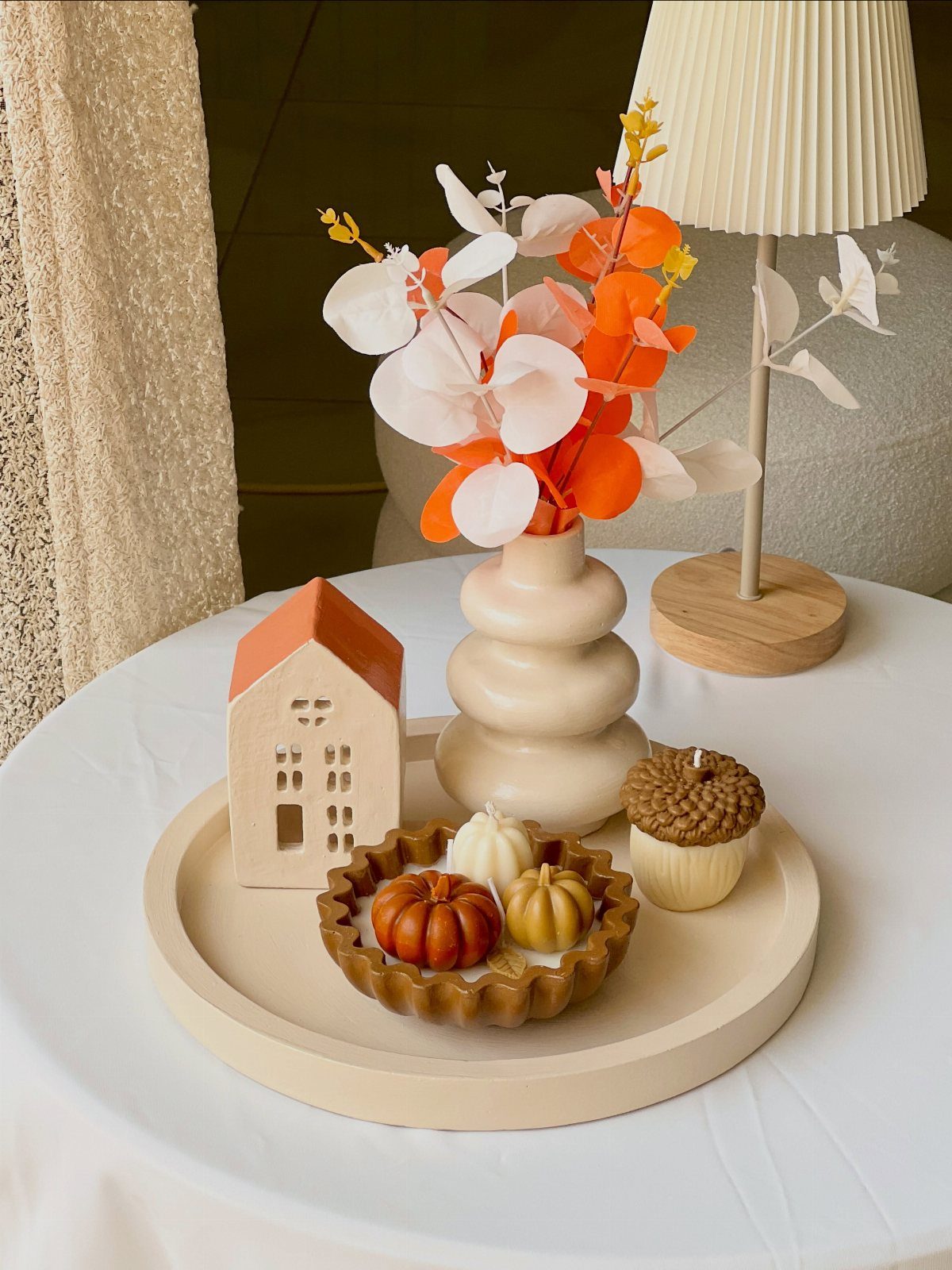 Decorative fall candles and a ceramic house on a tray atop a white table.
