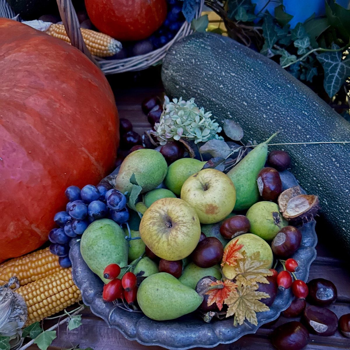 Assorted autumn fruits and vegetables including pumpkins, pears, apples, and grapes in a bowl.
