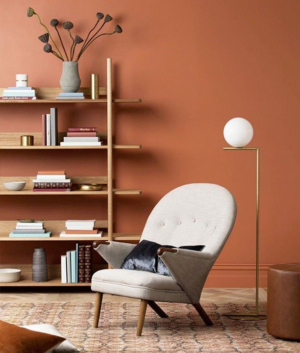 Cream armchair and wooden bookshelf set against a muted orange painted wall.