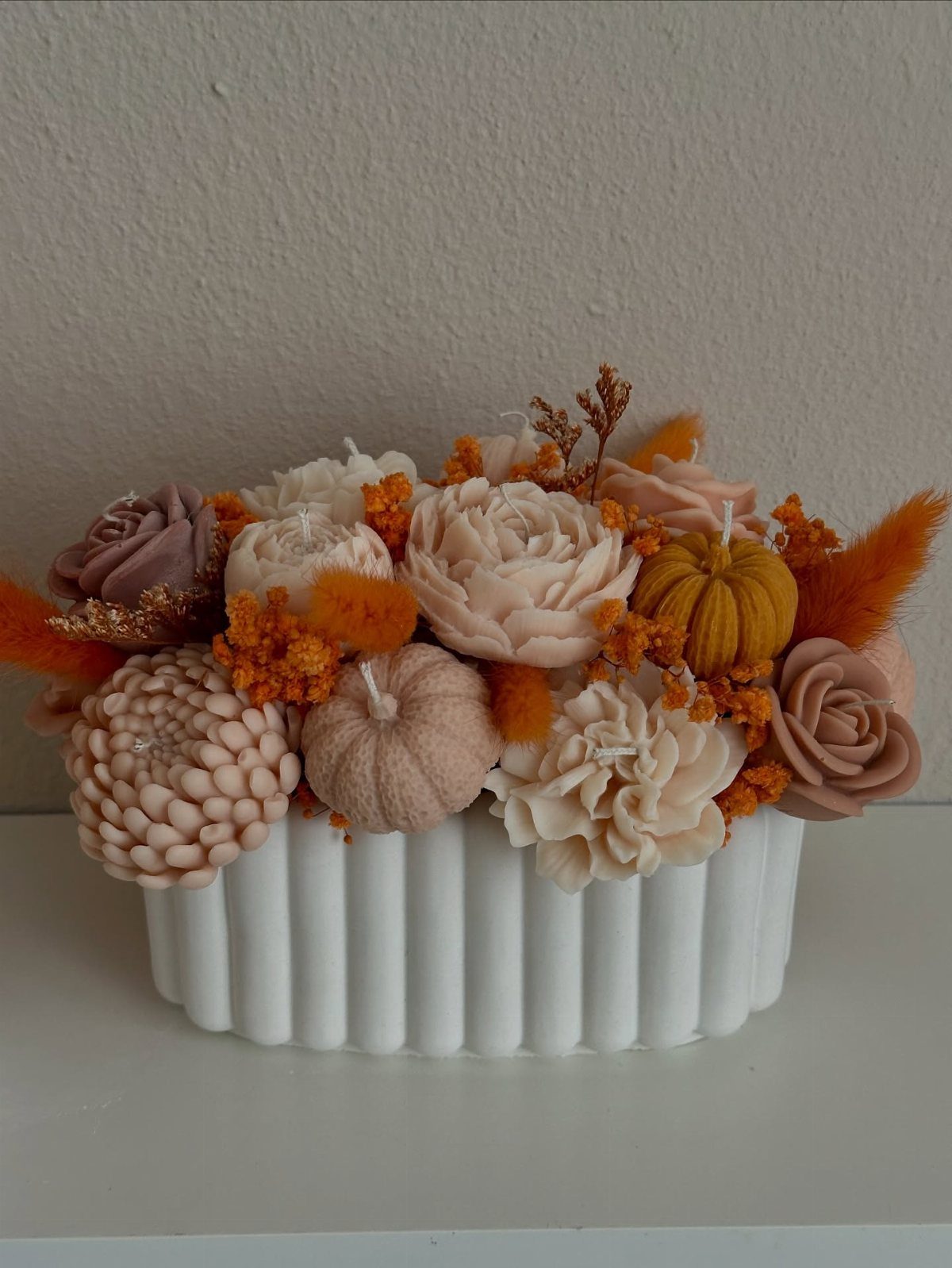 Decorative shaped candles in rose and pumpkin forms arranged inside a white fluted bowl.