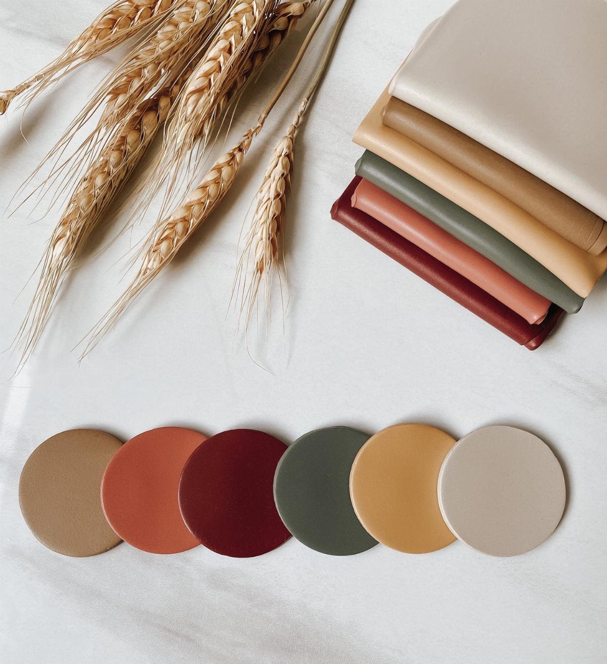 Dried wheat stalks, fabric swatches, and circular color palette samples in earthy autumn tones.