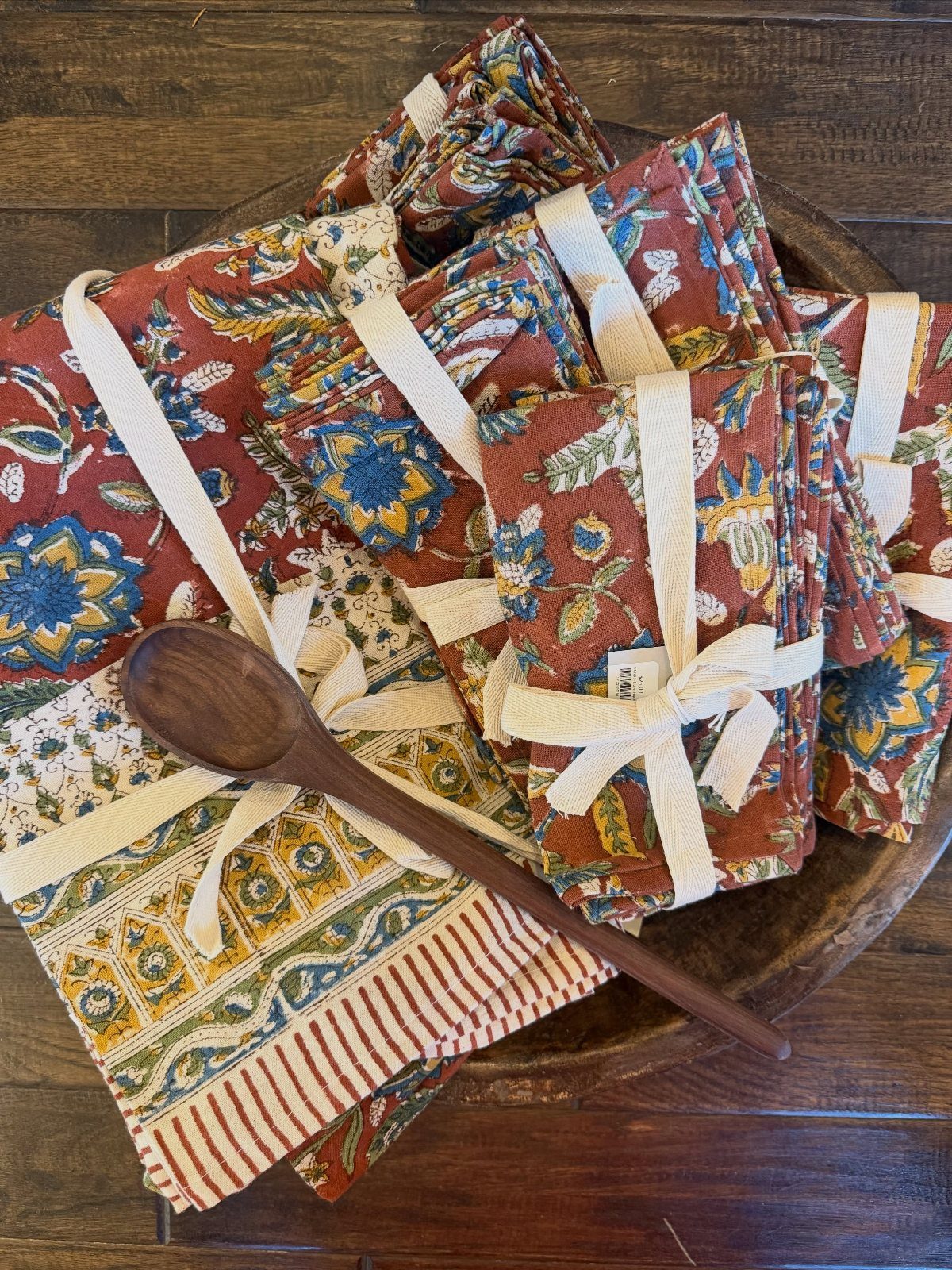 Patterned fabric napkins tied with cream ribbons resting in a wooden bowl with a wooden spoon.