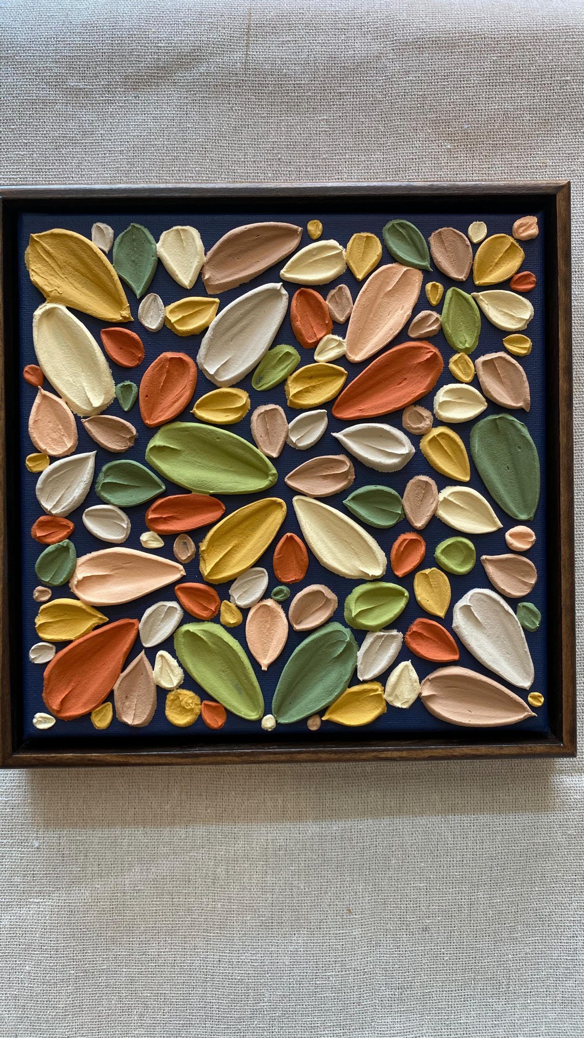 Textured leaf-shaped wall art in warm autumnal colors set against a dark blue background.
