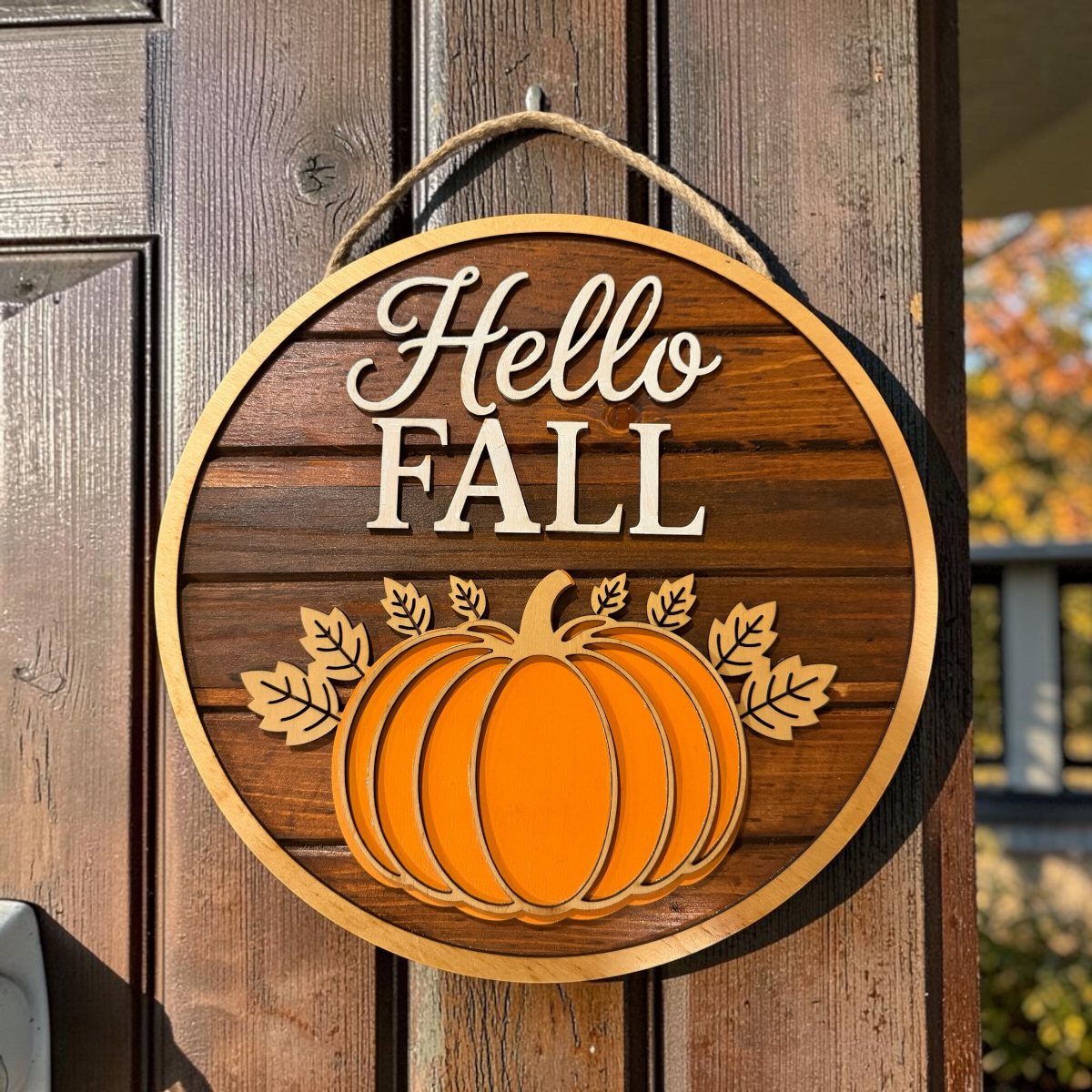 A circular wooden sign with a pumpkin and Hello Fall text hanging on a door.